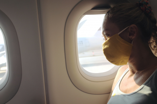 Woman Travel Caucasian At Plane With Wearing Protective Medical Mask. Girl Tourist At Aircraft With Protect Respirator
